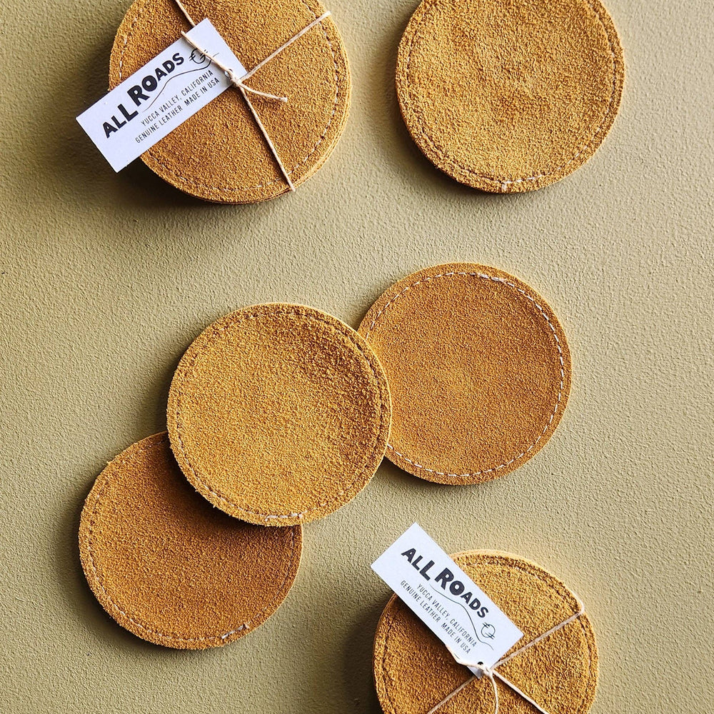 Set of round brown coasters with 'All Roads' labels on a beige background
