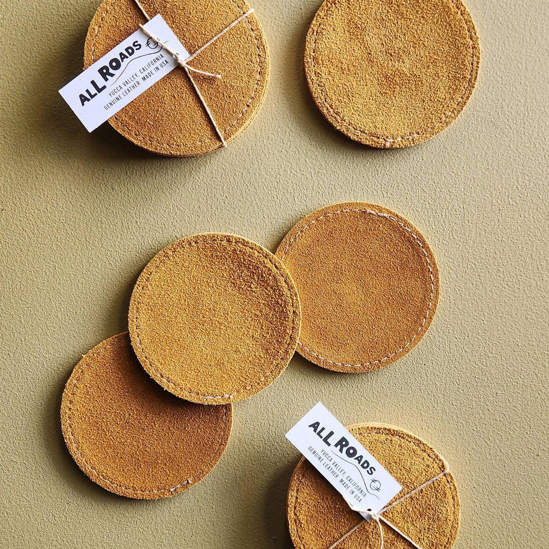 Set of round brown coasters with 'All Roads' labels on a beige background