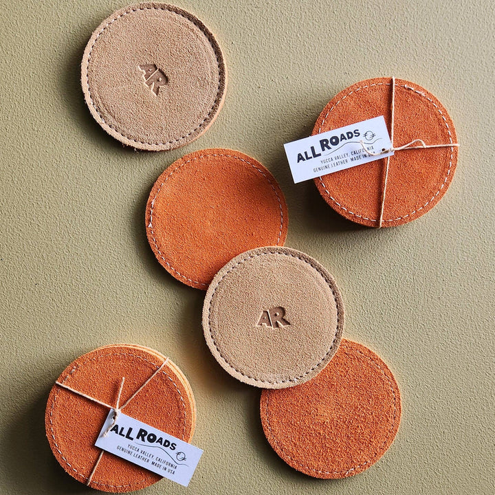 Round leather coasters with 'All Roads' branding on a beige background