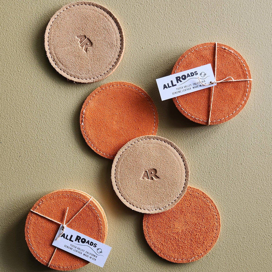 Round leather coasters with 'All Roads' branding on a beige background